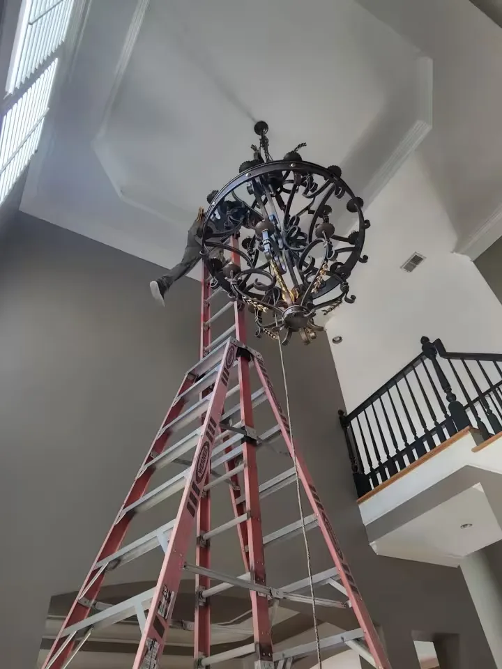 Technician on ladder installing a large wrought iron chandelier on a 20-foot ceiling in an Atlanta foyer