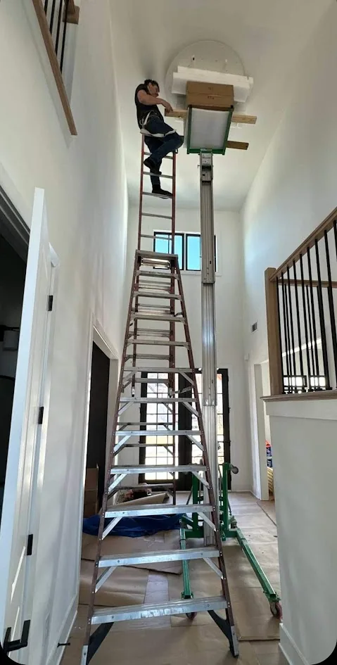 Technician using an extension ladder for stairwell chandelier installation in Atlanta